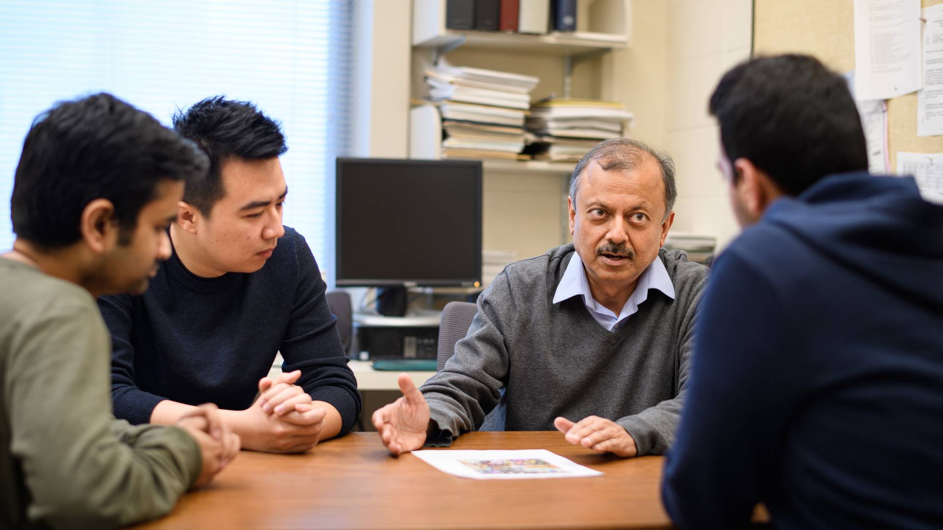 Jha Al speaks over a table to the students in his lab