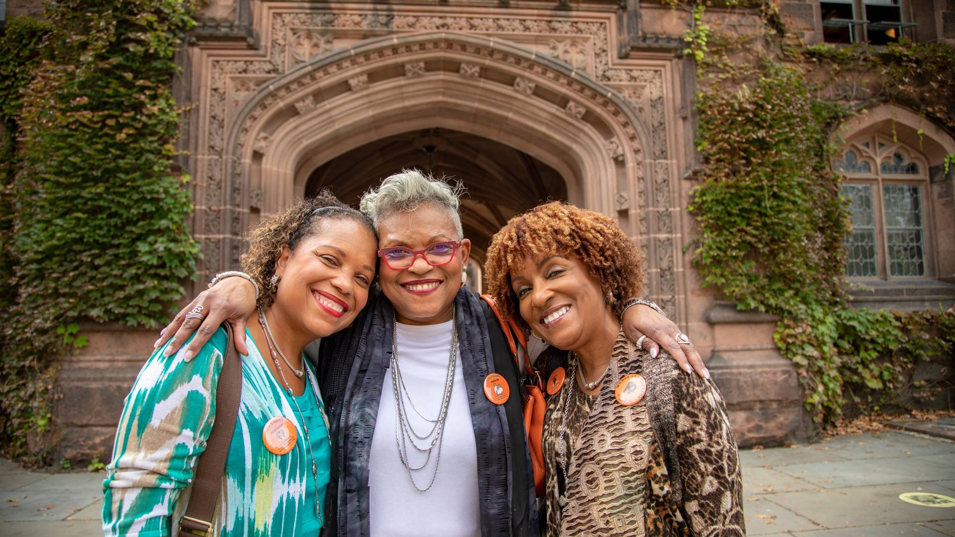 Three women stand and smiling on campus