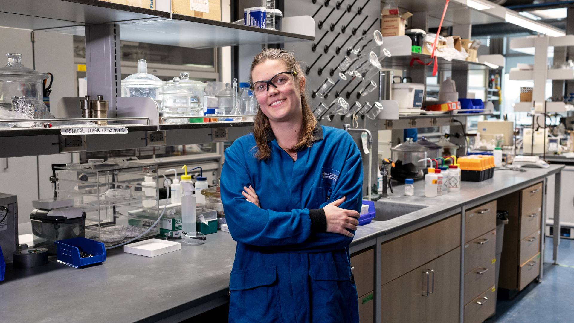 Leslie Schoop stands in her lab wearing a lab coat and safety glasses