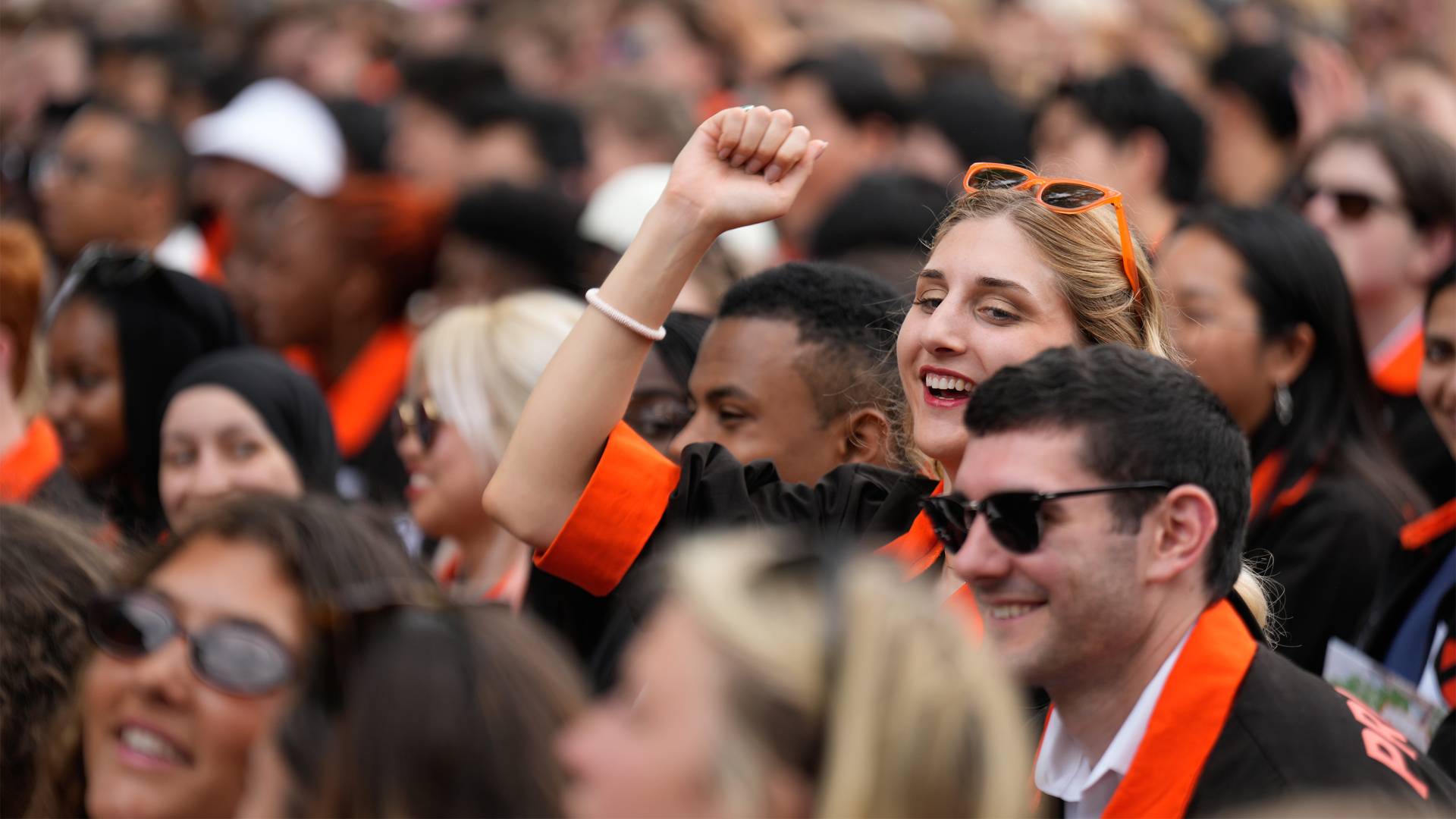 Graduating students in a crowd with one raising their fist in excitement