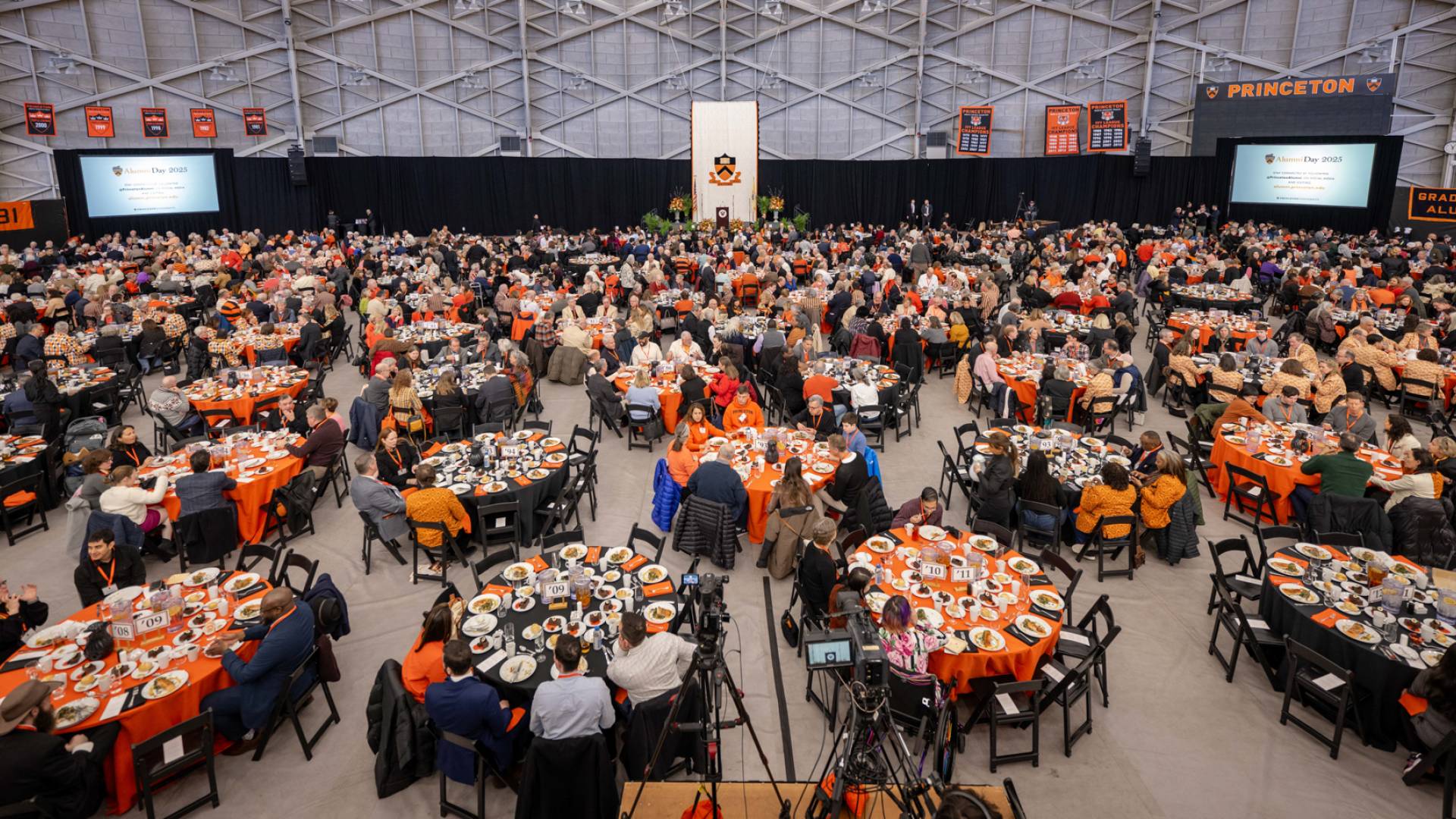 A large hall full of alumni seated around numerous tables.