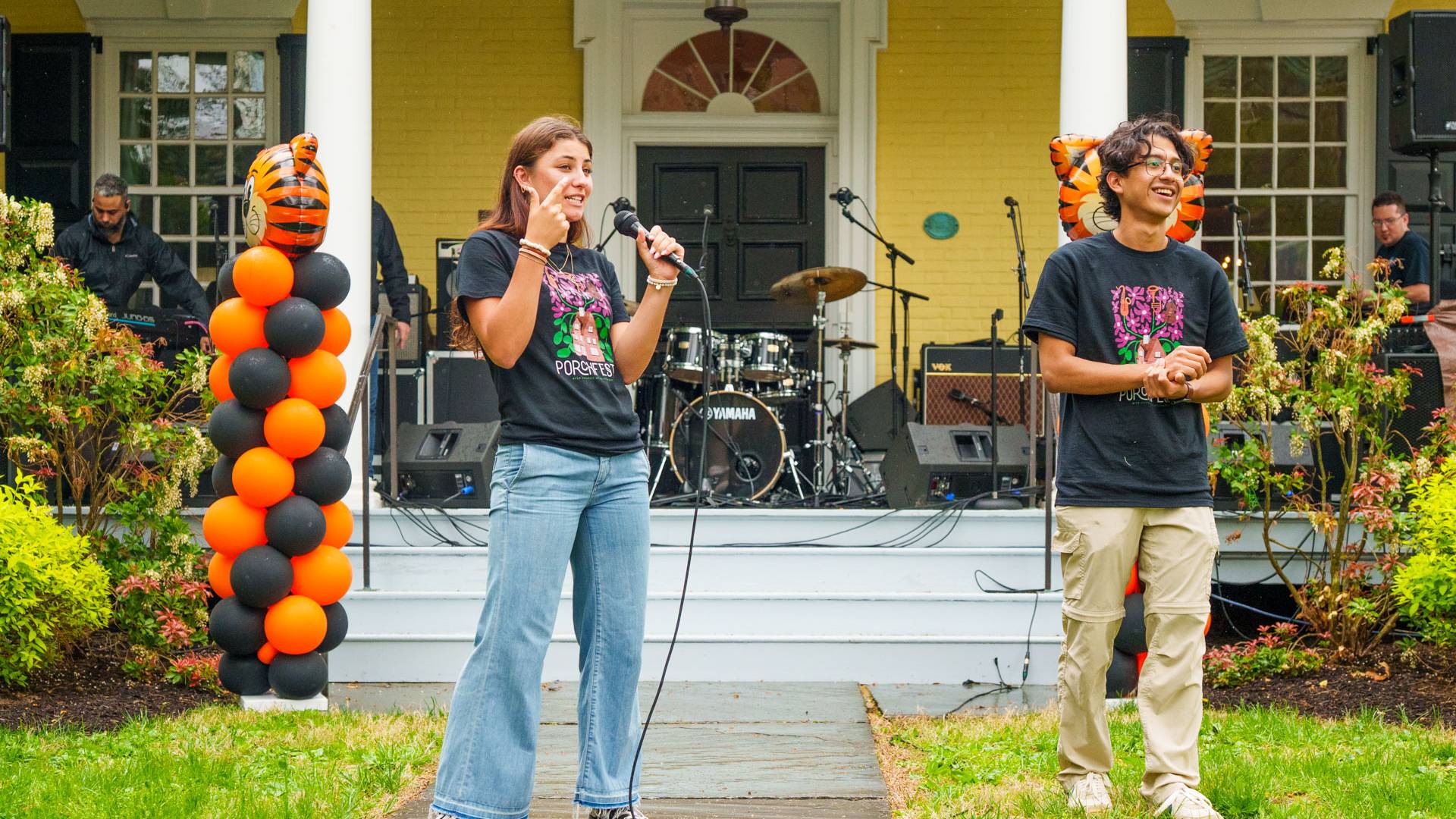 Two students hold microphones on the lawn of Maclean House on campus.