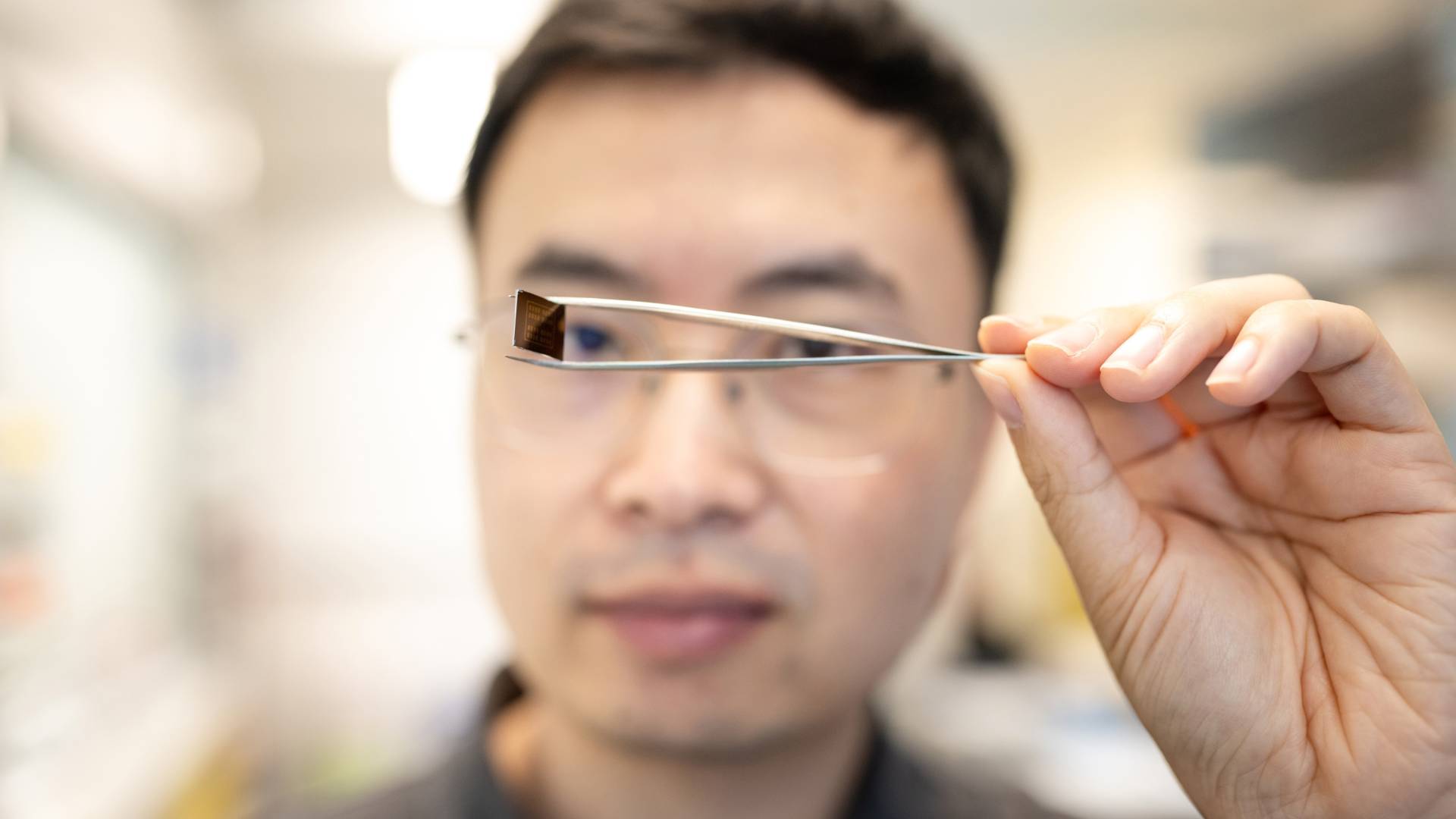 A researcher holds a small semiconductor up to his eye to examine it.