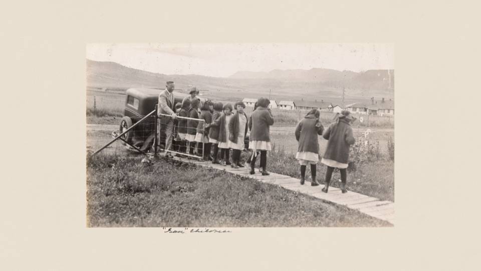A man with a row of identically dressed girls on a narrow wooden boardwalk