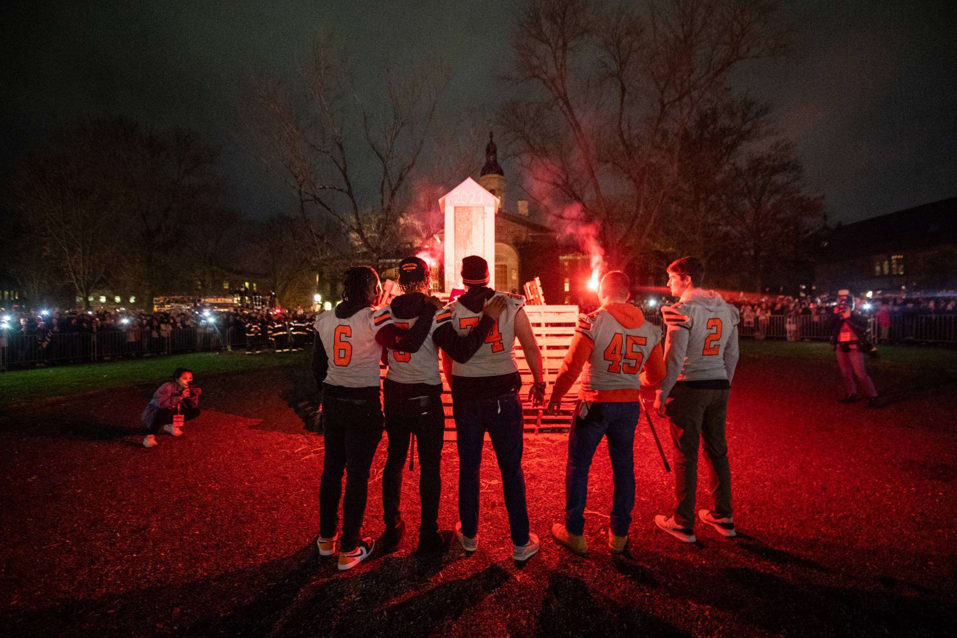football players in their jerseys light the bonfire