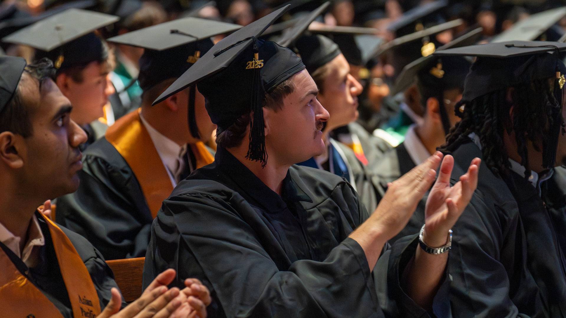 Students in caps and gowns applaud.