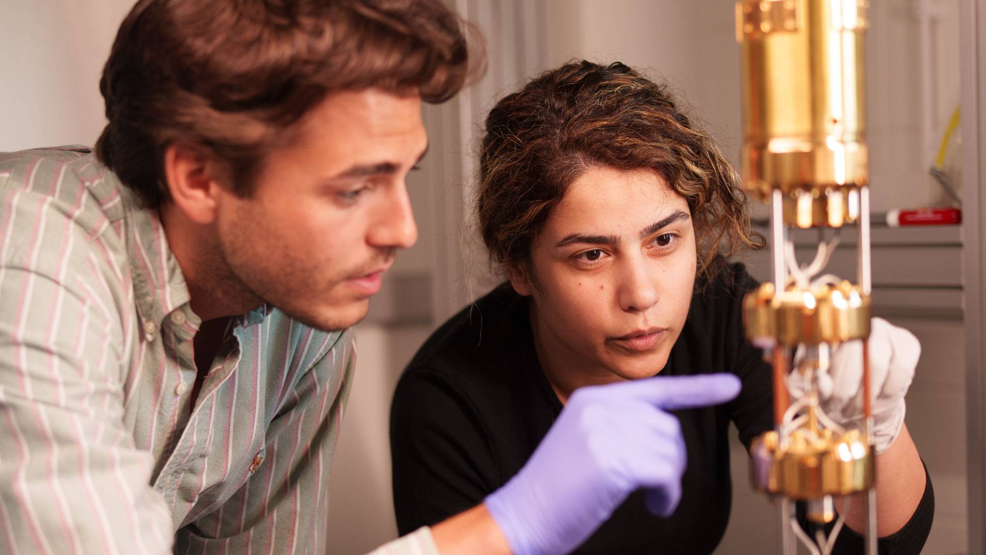 Two people stare intently at a complex golden apparatus.
