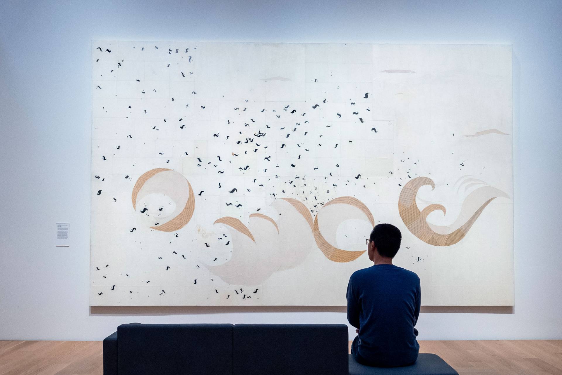 Scientist Ben Zhang sits on a bench and looks at an abstract painting.