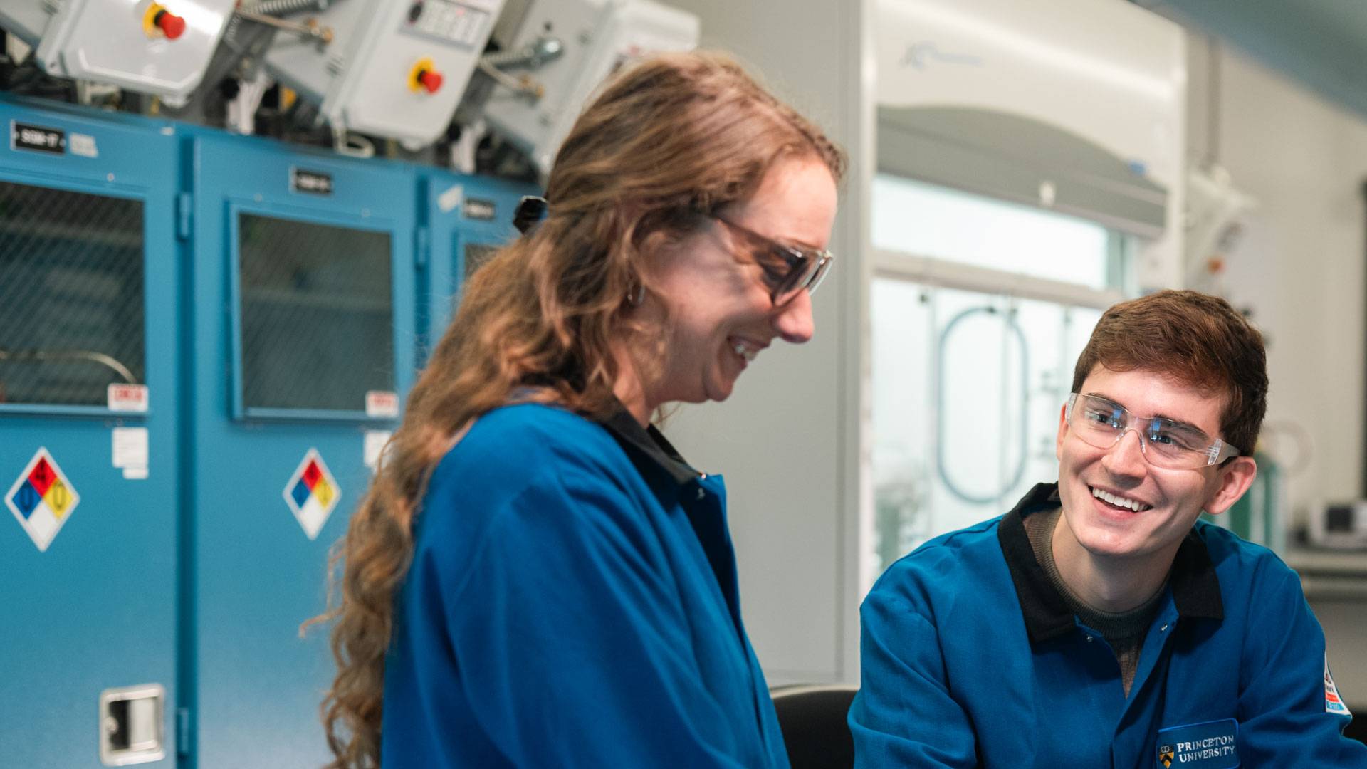 Two individuals wearing lab coats inside a lab.