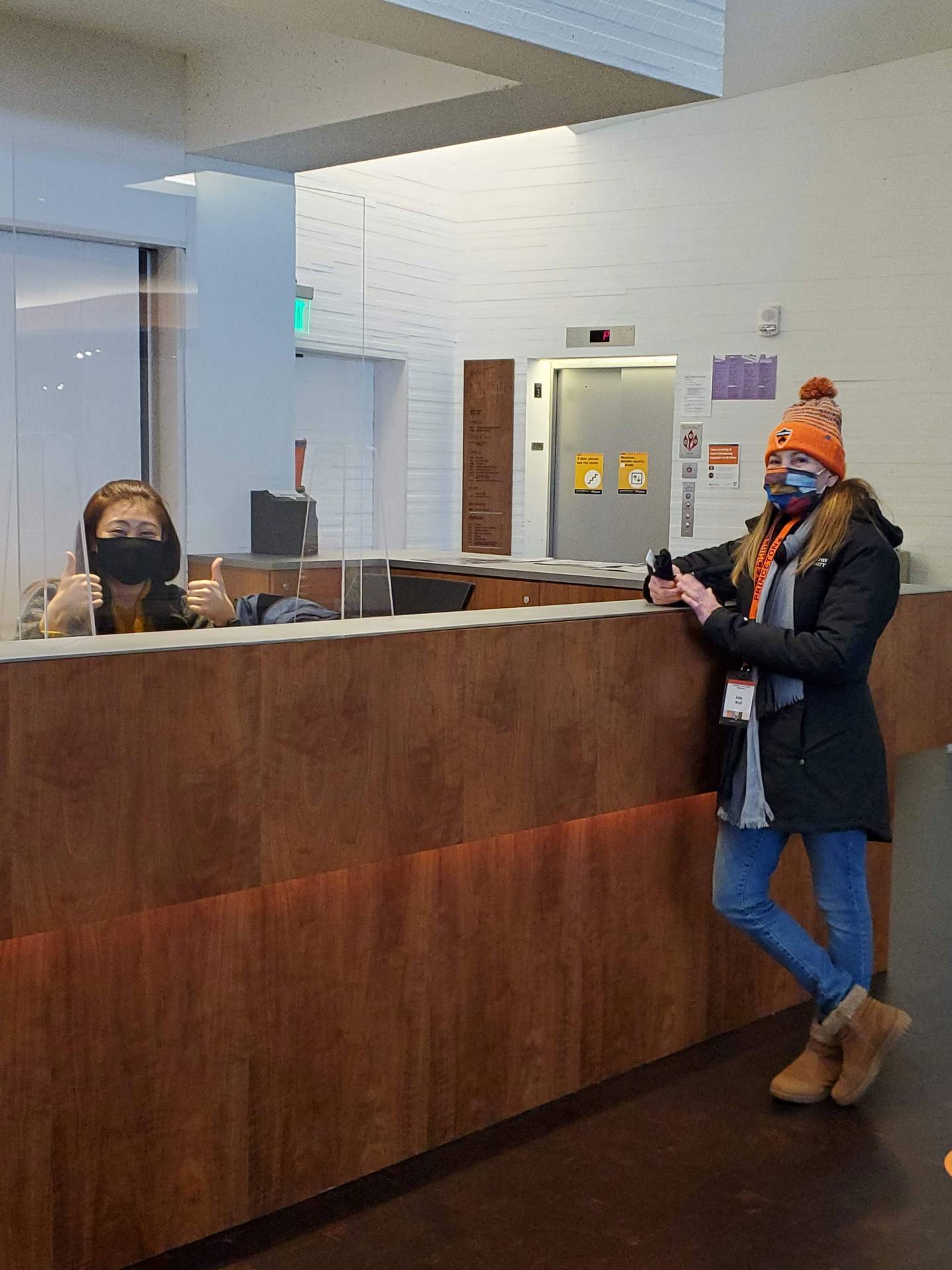 A student in front of a reception area, receptionist smiling and giving thumbs up signal