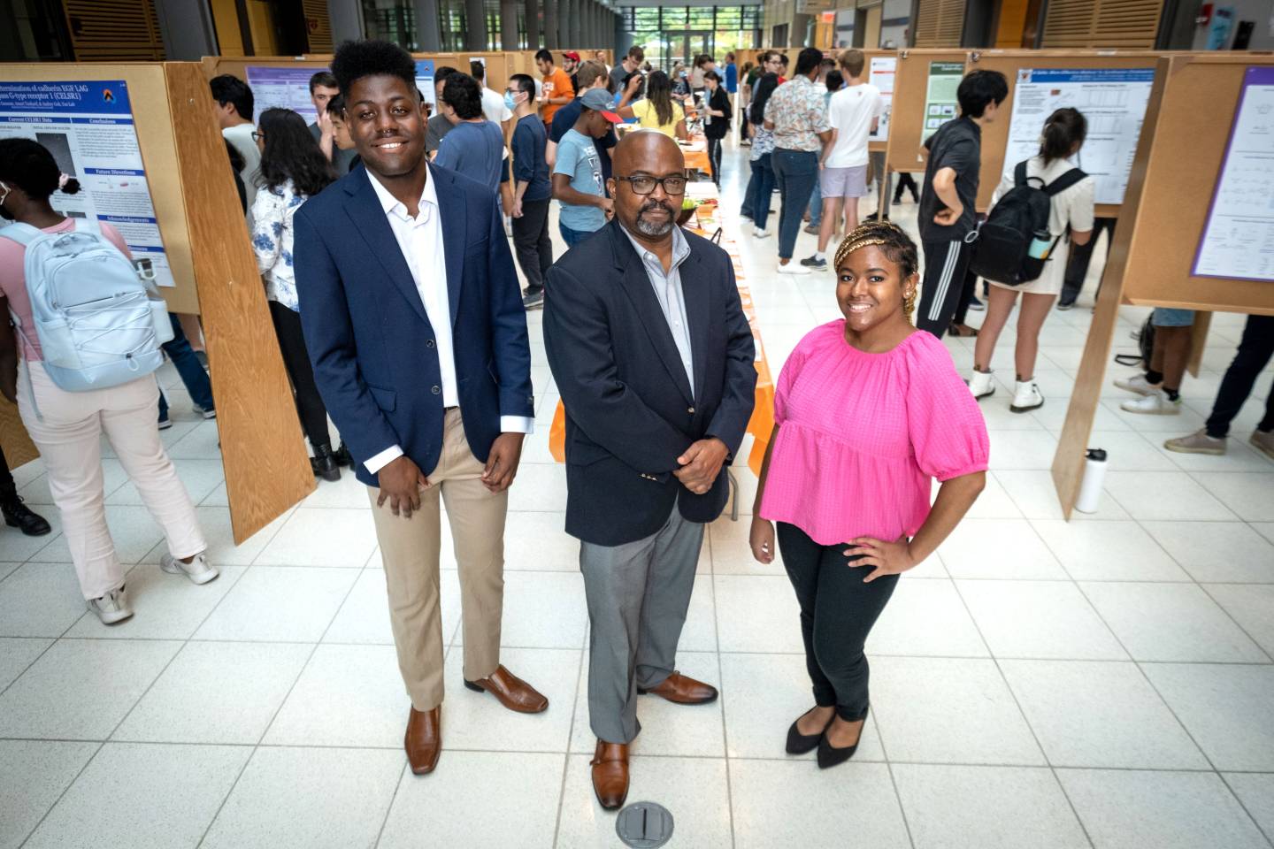 A visiting professor and his 2 students in a space where others are presenting research posters
